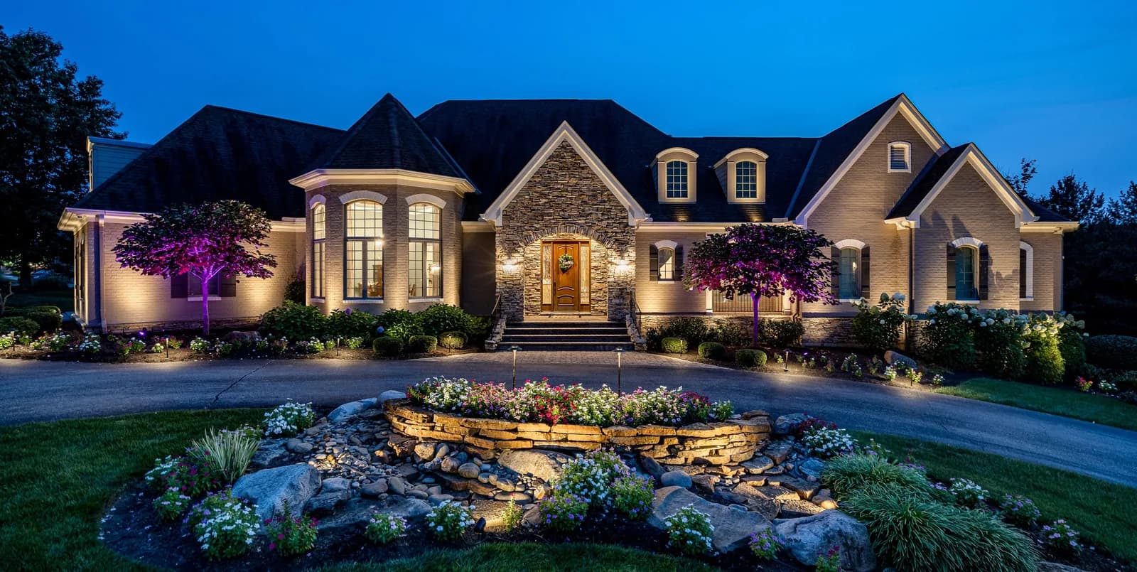 Home with white landscape uplighting on trees, beds and façade